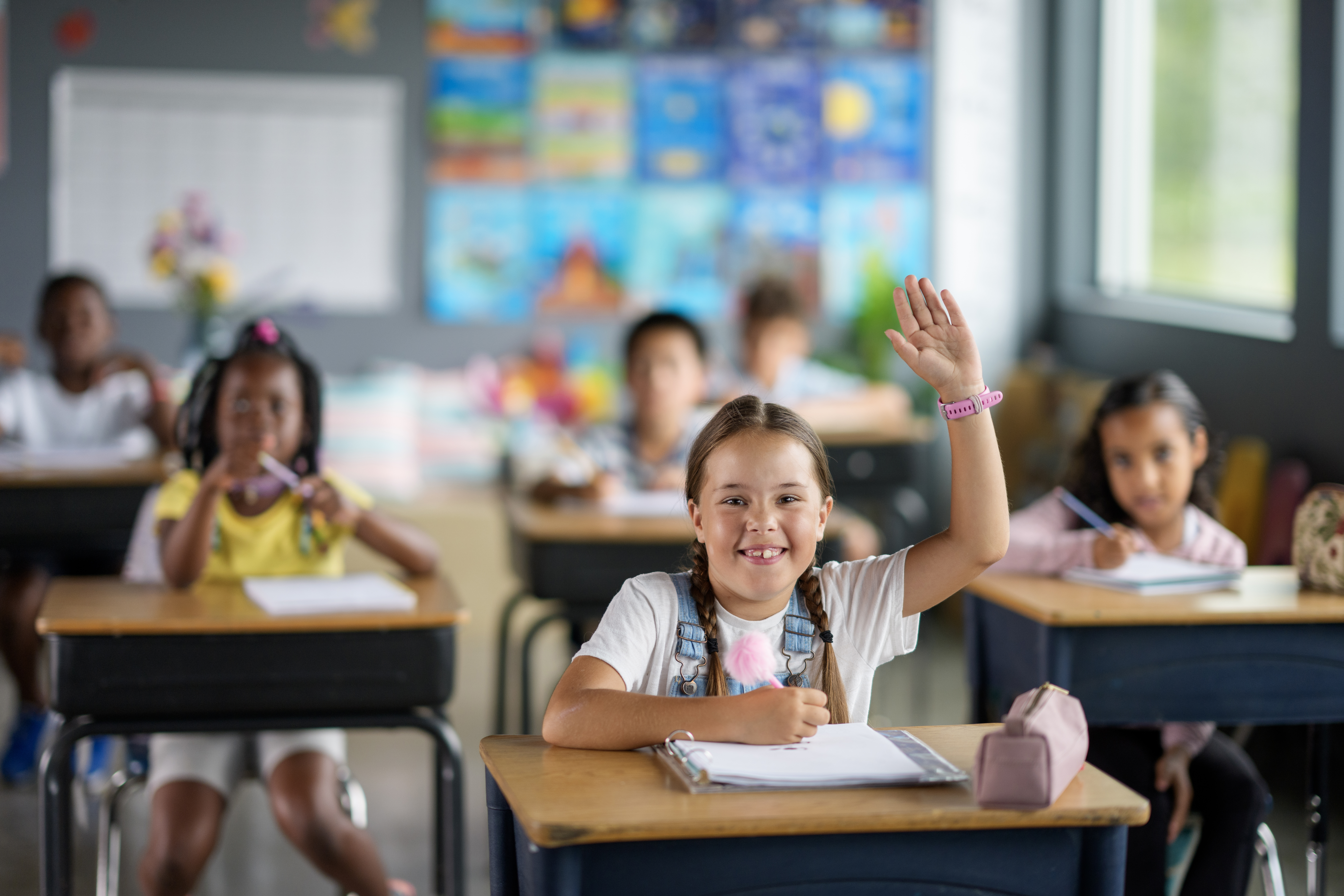 Group of students participating in a classroom with one raising their hand.